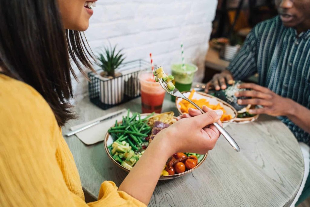 Woman enjoying colorful Buddha bowl with vegetables and smoothies at restaurant table