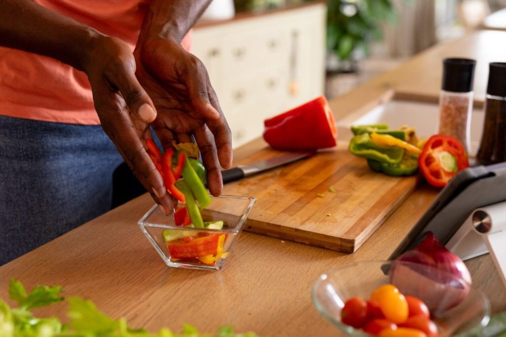 Person slicing colorful bell peppers on wooden cutting board in bright kitchen