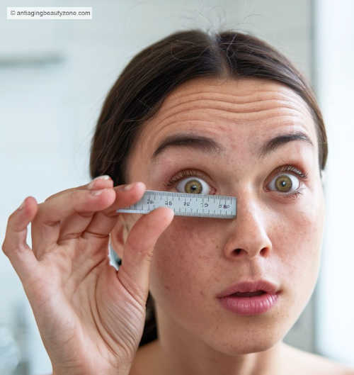 How to Find Your Eye Shape & Apply Makeup That Flatters Woman using a ruler to measure her eye shape, demonstrating how to determine eye type for optimal makeup application.